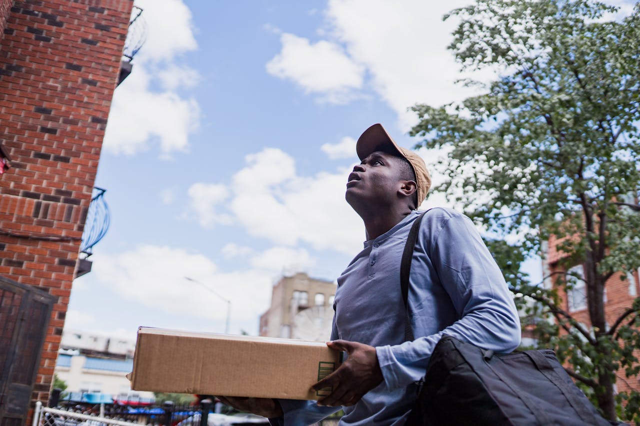 home-hero-bg Man delivering a package in a city neighborhood, looking up at the building.